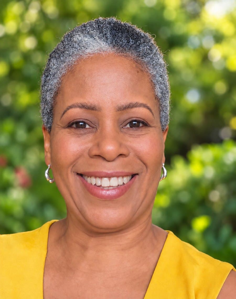 Lorraine Villaroel, smiling, in a yellow top against a leafy garden